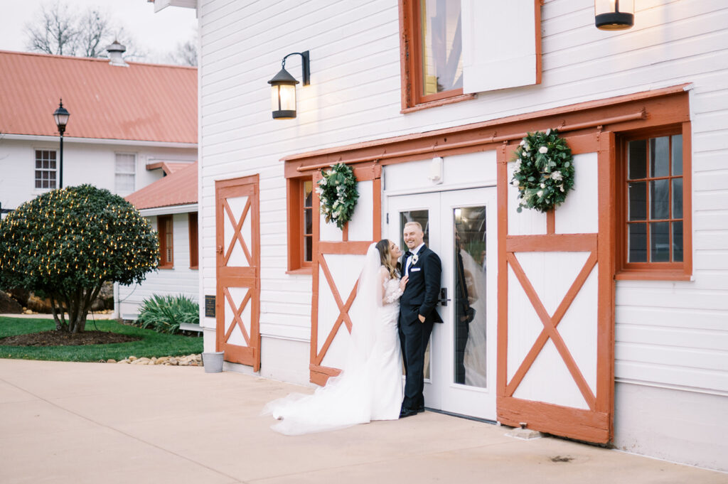 A bride and groom in front of WinMock at a holiday wedding with Christmas wreaths attached to the doors.